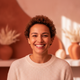 Close-up portrait of a happy woman in her 30s, smiling genuinely, against a soft background in warm terracotta and burnt sien
